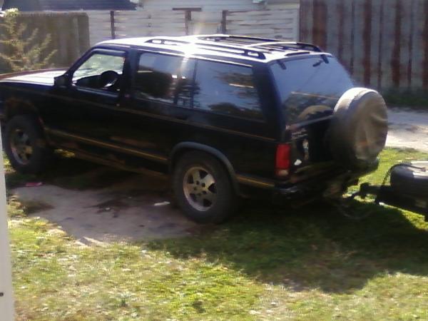 black SUV parked outside, spare tire mounted on rear door, towing a small trailer