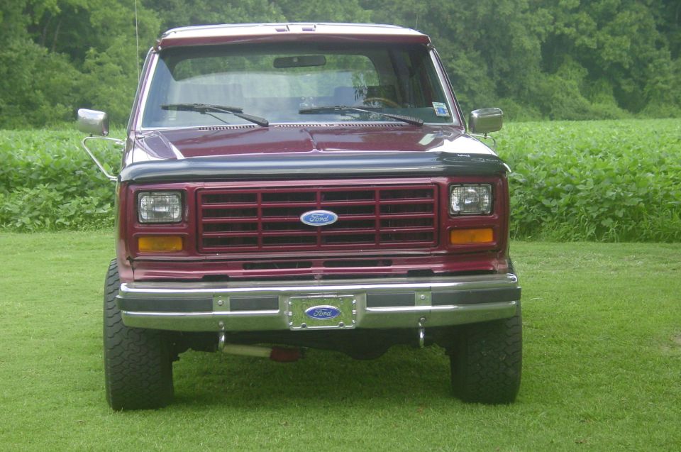 Front view of a lifted maroon Ford Bronco with chrome bumper and hood deflector parked on grass