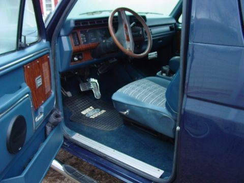 1984 Ford Bronco - The interior of a blue SUV features a patterned seat and wood-grain accents on the dashboard and door.