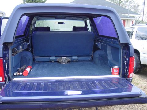 1984 Ford Bronco - The spacious cargo area of a blue 1984 Ford Bronco, complete with a fire extinguisher and a can of oil. Another SUV is visible to the right.