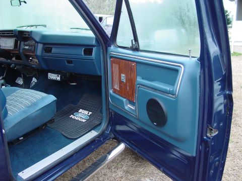 1984 Ford Bronco - Interior view of a 1984 Ford Bronco, blue upholstery and a "Built Ford Tough" floor mat.