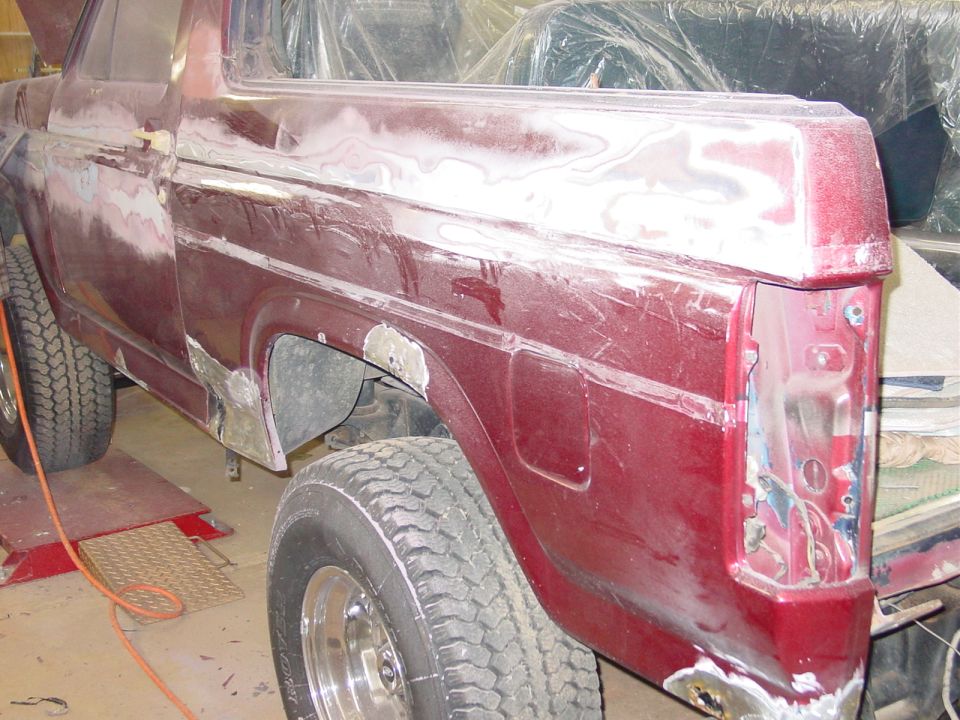 Side view of a red Ford Bronco body being prepped for paint, showing body filler and primer