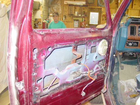 1984 Ford Bronco - The interior of a maroon vehicle shows exposed door mechanisms and a blue dashboard, with a man visible in the background.
