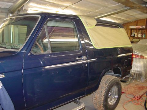 1984 Ford Bronco - A dark blue SUV, likely from the early 1980s, is parked indoors with a protective cover on its rear window.