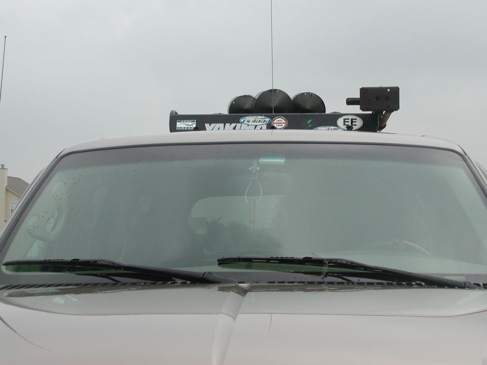 Silver SUV front windshield with roof-mounted light bar and off-road lamps under gray sky