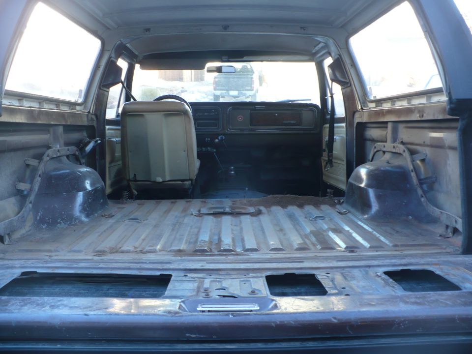 Interior view of an old SUV, looking from the cargo area towards the front seats and dashboard. The cargo area is empty and shows metal flooring