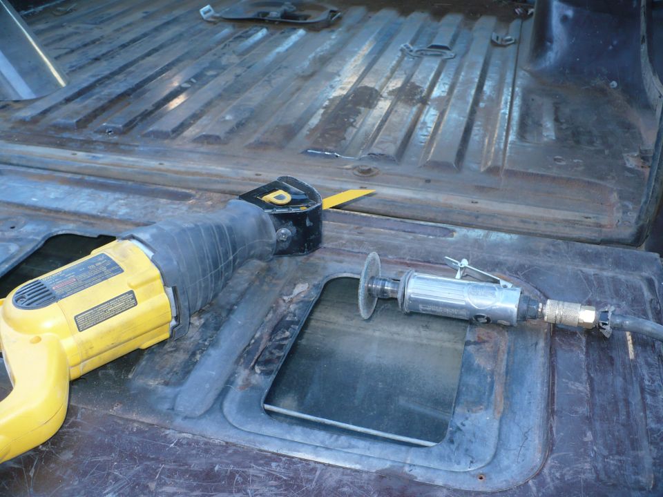Reciprocating saw and angle grinder on a rusty, ribbed metal floor with cutouts