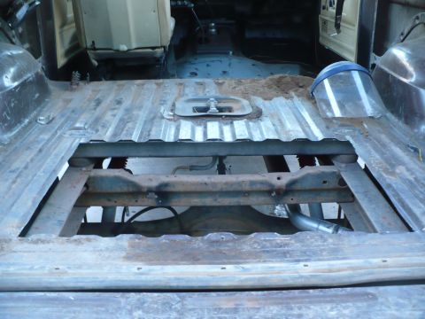 1979 Ford Bronco - The interior floor of a vehicle shows exposed chassis components and an exhaust pipe, with a face shield nearby.