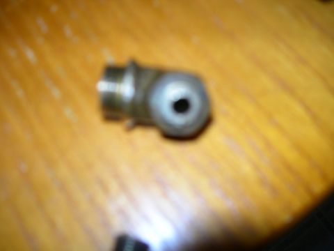1984 Ford Bronco - A metal fitting, possibly a grease zerk or adapter, rests on a wooden surface. The registry claims it is from a 1984 Ford Bronco.