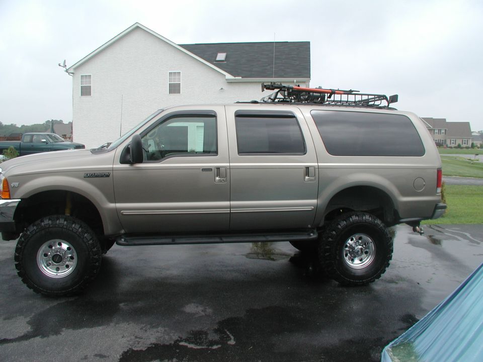 Side view of lifted tan Ford Excursion on large off-road tires with roof rack