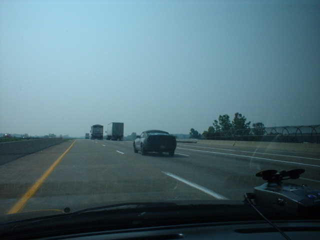 Car on highway with trucks ahead and to the side under a hazy sky
