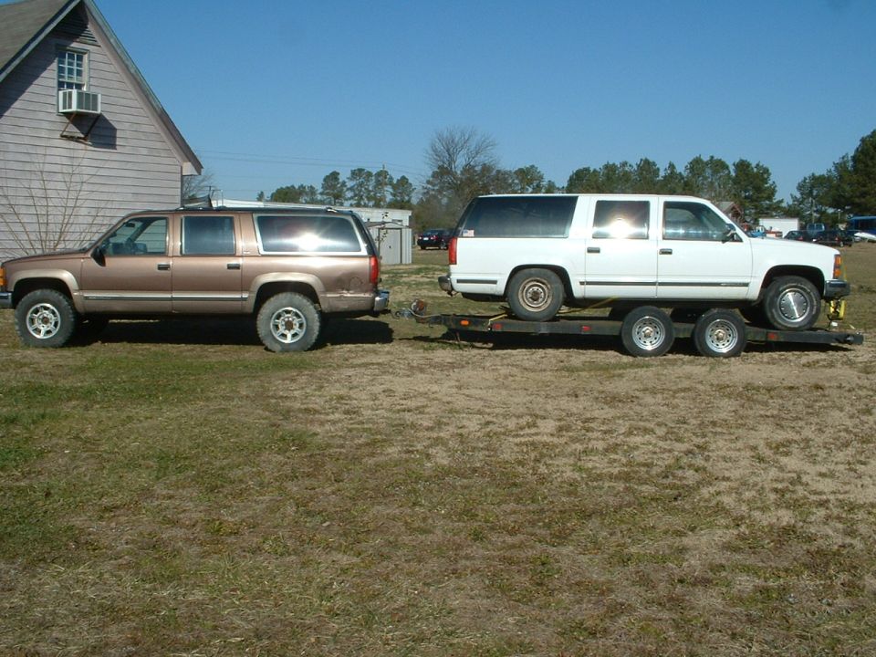 Brown and white Suburbans, one towing a trailer with a white Suburban