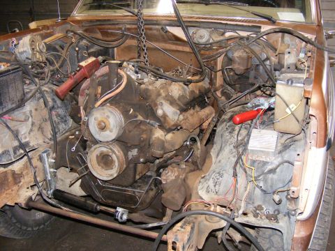 1985 Ford Bronco - The engine bay of a 1985 Ford Bronco is shown with the engine partially removed, revealing its internal components and wiring.
