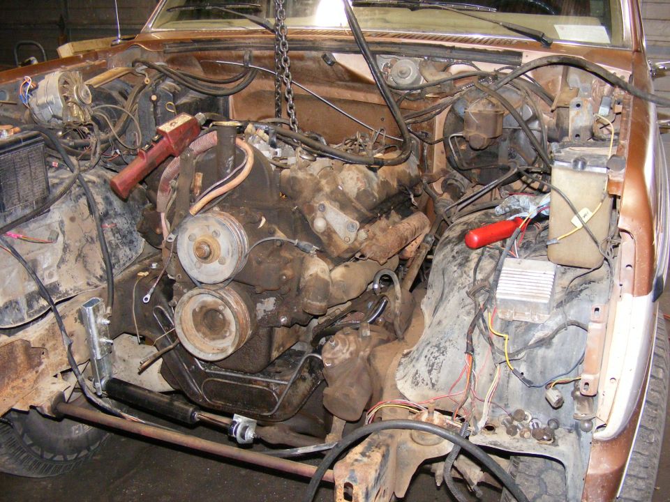Brown 1985 Ford Bronco engine bay with engine removed, showing rusty components and wiring