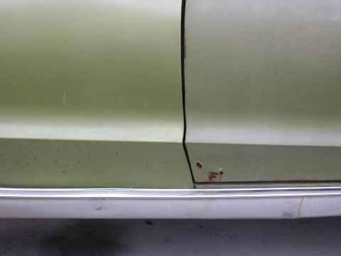 1968 Mercury Cougar - Detail of a green car's door seam, showing signs of rust and chrome trim along the lower edge.