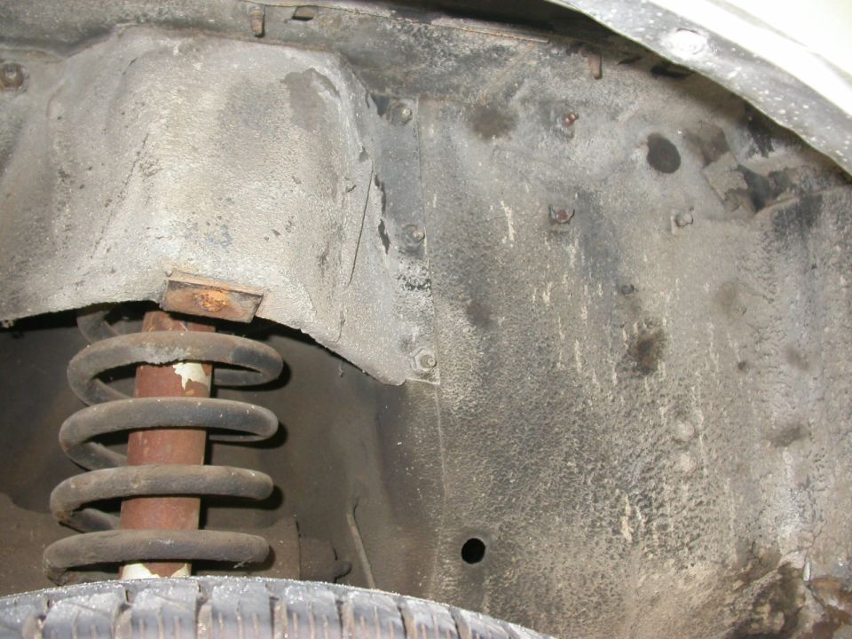 Wheel well interior with coil spring and tire visible. Rusty metal and textured undercoating