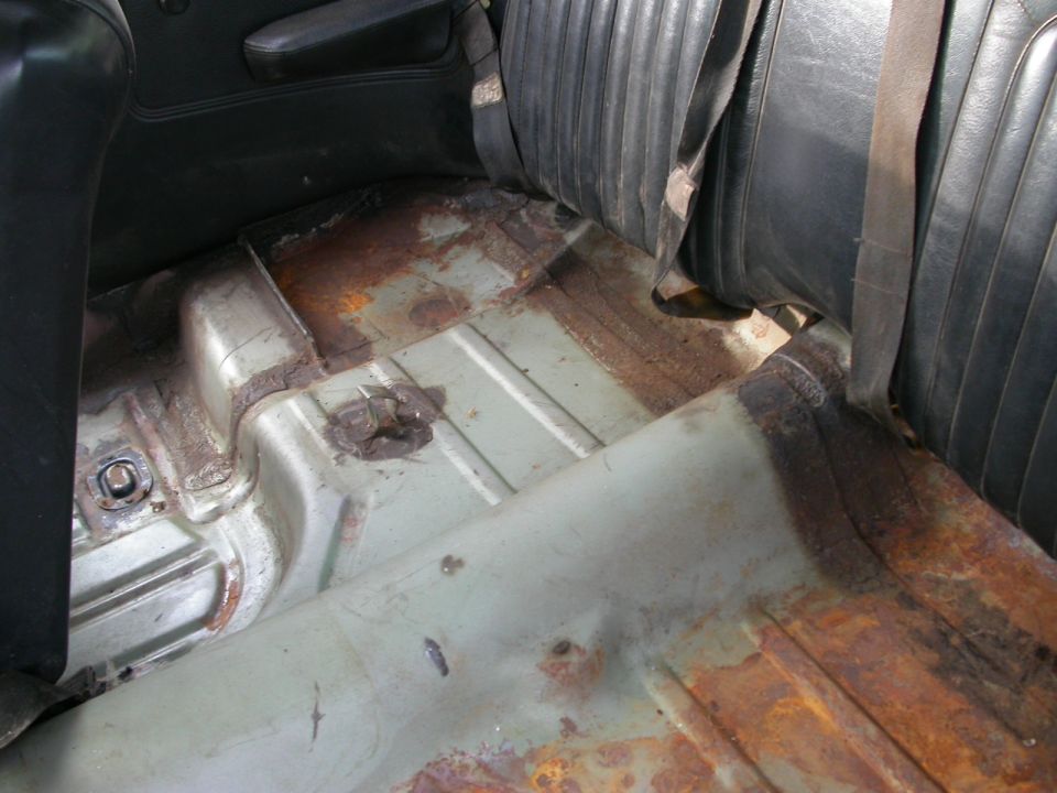 Interior view of a car's floor pan showing significant rust damage