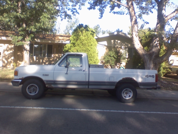 Side view of a white 1991 Ford F-150 pickup truck parked on a street