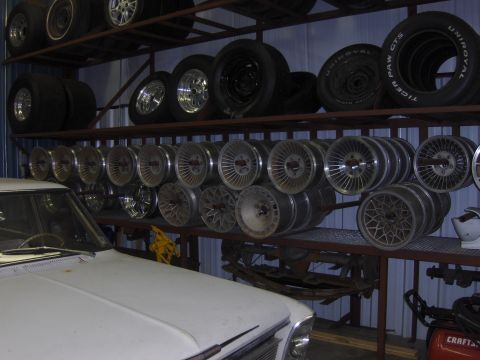 1979 Chevrolet Camaro - A storage area displays shelves packed with various tires and custom car wheels, with the hood of a white vehicle visible.