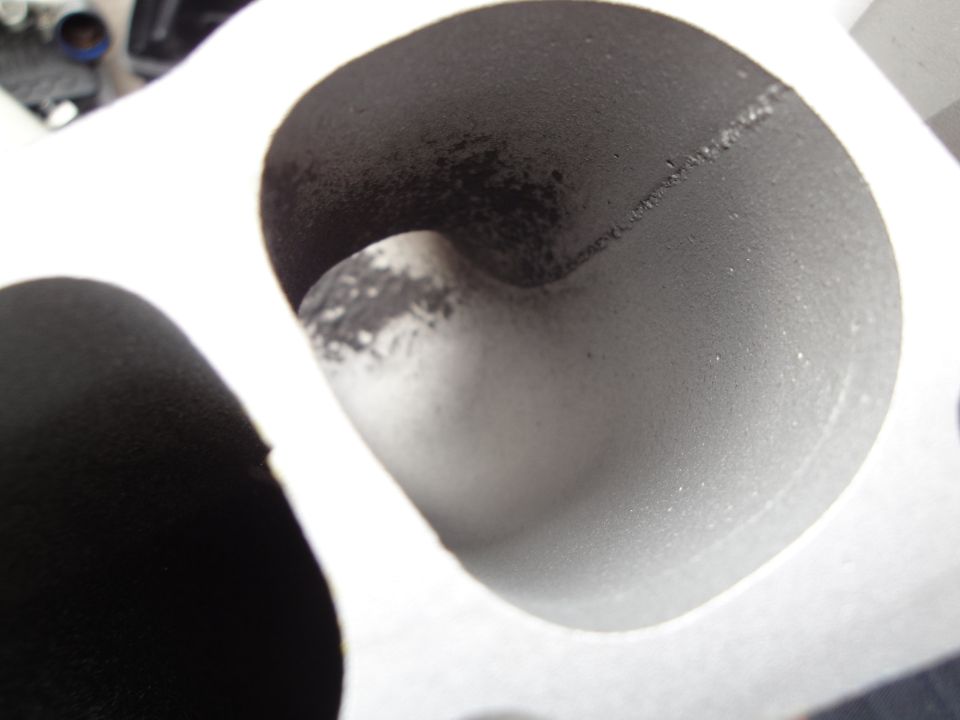 Close-up of a dusty engine intake manifold port with a visible weld seam