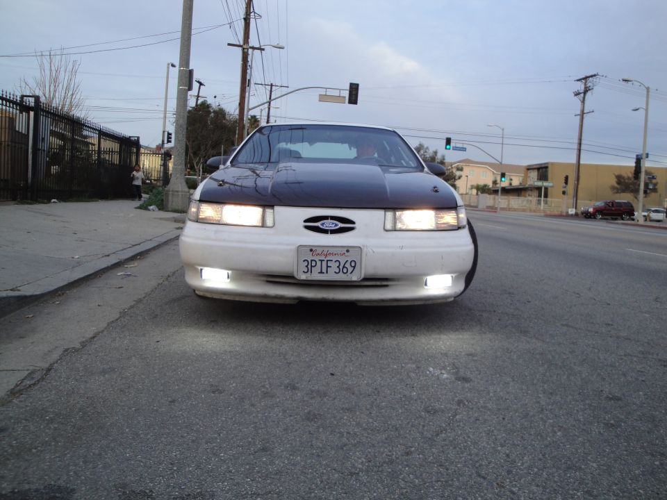 Front view of a white Ford Taurus with a black hood and a California license plate reading 3PIF369