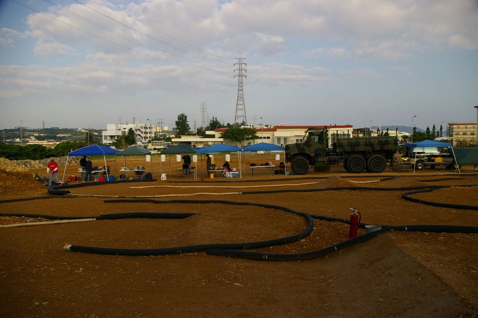 Dirt RC track with pit canopies and a camouflage 6x6 military cargo truck parked behind