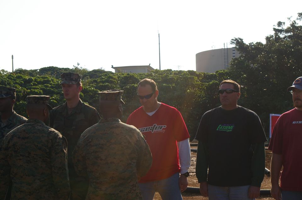 Group of people in uniforms and casual wear outdoors, with a large cylindrical structure in the background