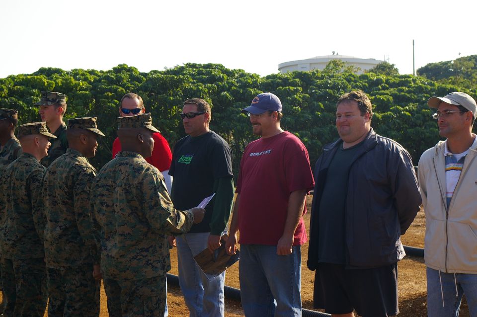 Marines in formation receiving something from a civilian. Others in civilian clothes stand behind them