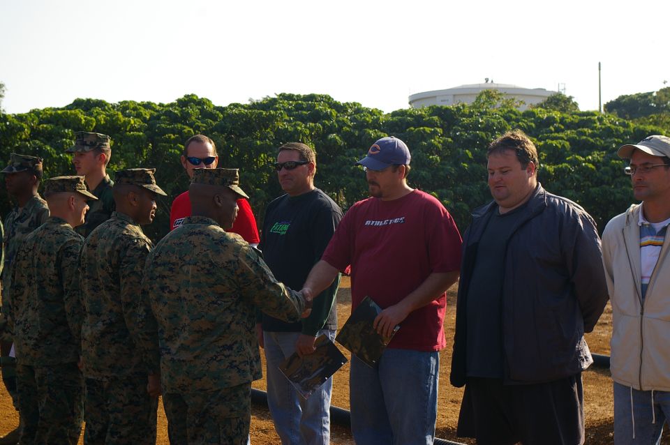 Marines and civilians gathered outdoors, with a water tower in the background