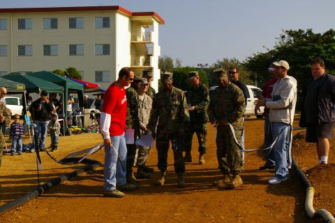 1986 Ford Bronco - A group of people, some in military uniforms, are gathered outdoors near tents and a building.