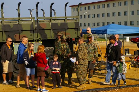 1986 Ford Bronco - A group of people, some in military uniform and others in civilian clothes, gather around a large military vehicle.