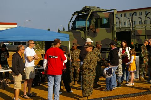 1986 Ford Bronco - A group of people, some in military uniform, stand around a large camouflage truck under a blue tent.