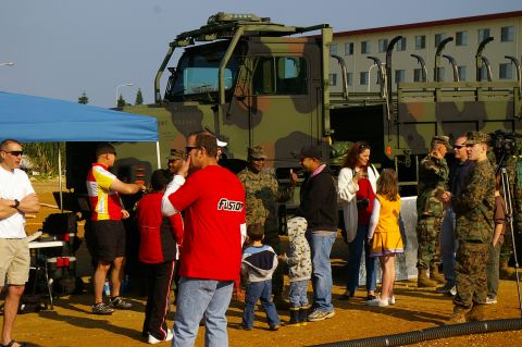 1986 Ford Bronco - A group of people, including civilians and military personnel, stand around a large military truck.