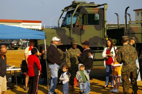 1986 Ford Bronco - A group of people, including Marines and civilians, stand near a camouflage military truck.