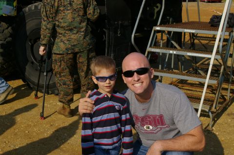 1986 Ford Bronco - Man and child pose with military personnel and a large vehicle tire in the background.