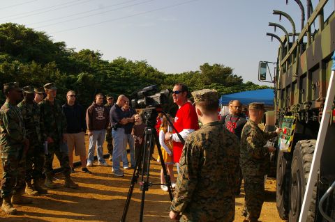 1986 Ford Bronco - A group of people, including military personnel and a camera crew, are gathered near a large, camouflaged truck.