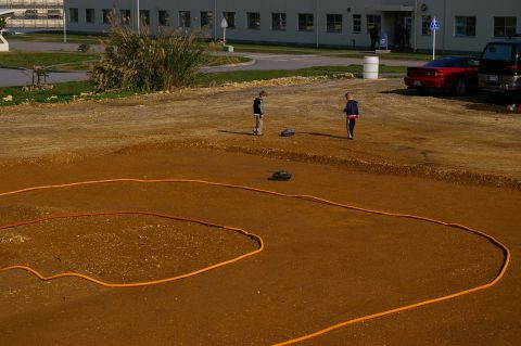 1986 Ford Bronco - Children observe remote control cars on a dirt track marked by an orange hose.