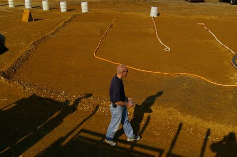 1986 Ford Bronco - A man walks across a dirt lot, casting a long shadow in the afternoon sun.