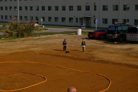 1986 Ford Bronco - Two children interact with a remote control car on a dirt track, with a large building visible in the background.