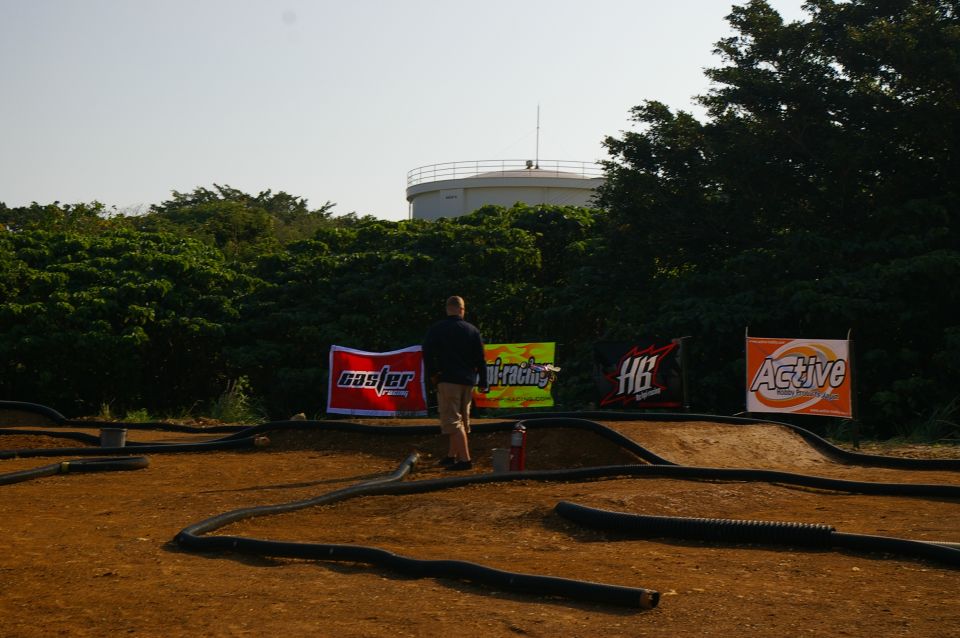 RC car track with black tubing borders and sponsor banners reading 'caster', 'vi-racing', 'HB', and 'Active'. Water tower in background
