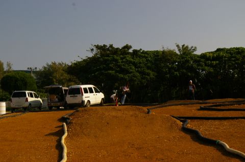 1986 Ford Bronco - A scene of a dirt track with several vans parked nearby under a clear sky.