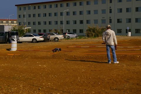 1986 Ford Bronco - A person watches a remote control car race on a dirt track in front of a large building.