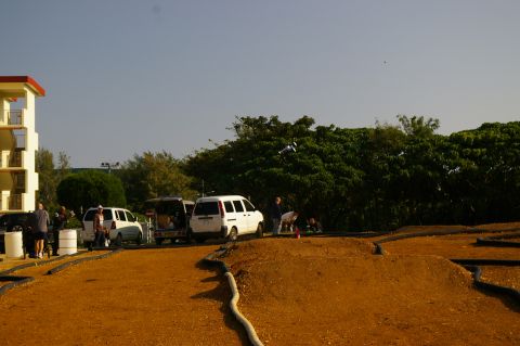 1986 Ford Bronco - RC airplane flying over a wooded area with parked vans and people.