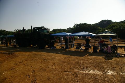 1986 Ford Bronco - A large military truck is parked at an outdoor gathering with several tents and people milling around.