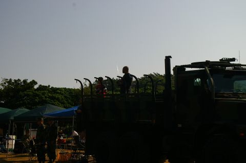 1986 Ford Bronco - People stand in the back of a military truck during an outdoor event with tents visible.