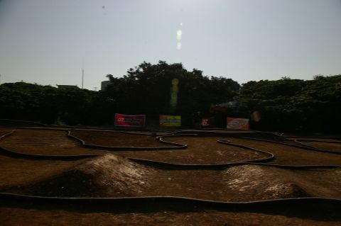 1986 Ford Bronco - An outdoor RC car track with various obstacles and sponsor banners is visible under a bright sky.