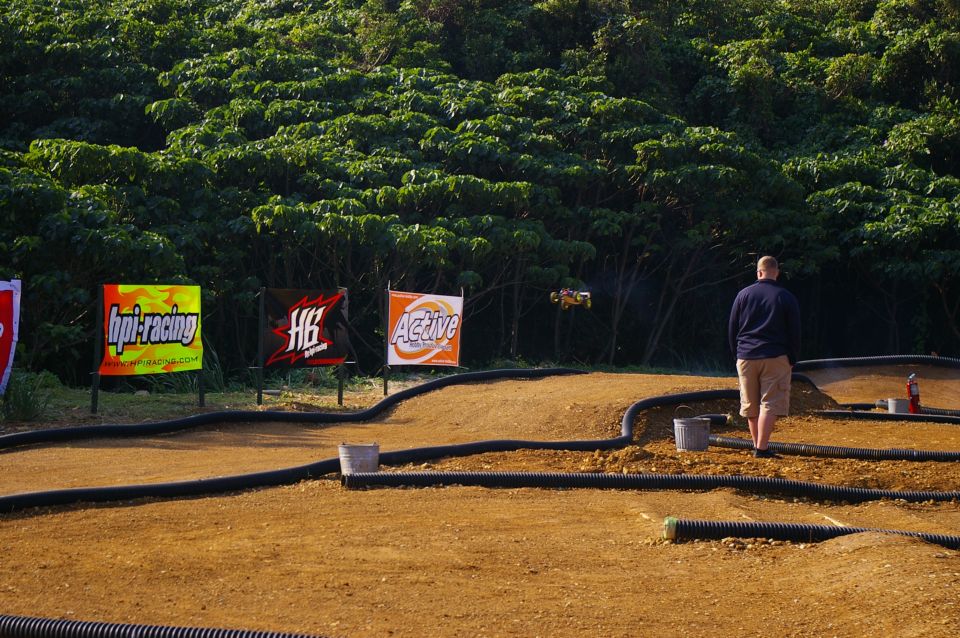 Remote control car mid-air over dirt track with HPI Racing and Active banners in background