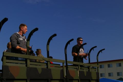 1986 Ford Bronco - Two men stand in the back of a camouflage military truck under a clear blue sky.