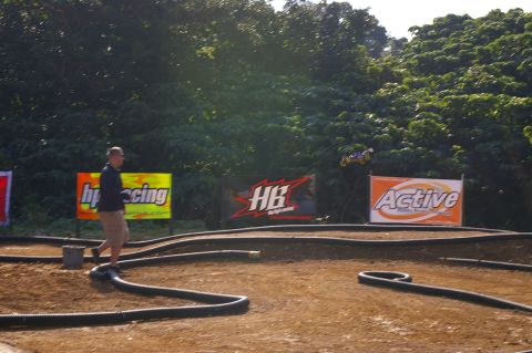 1986 Ford Bronco - A remote control car is airborne at a dirt track event with sponsor banners visible.