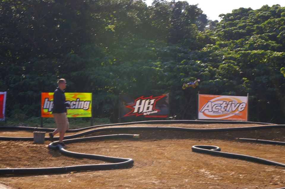 Remote control car mid-air over a dirt track with sponsor banners in the background